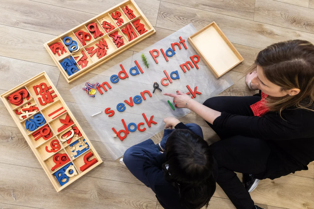 ALT "A Montessori teacher is helping her student with spelling and building words."